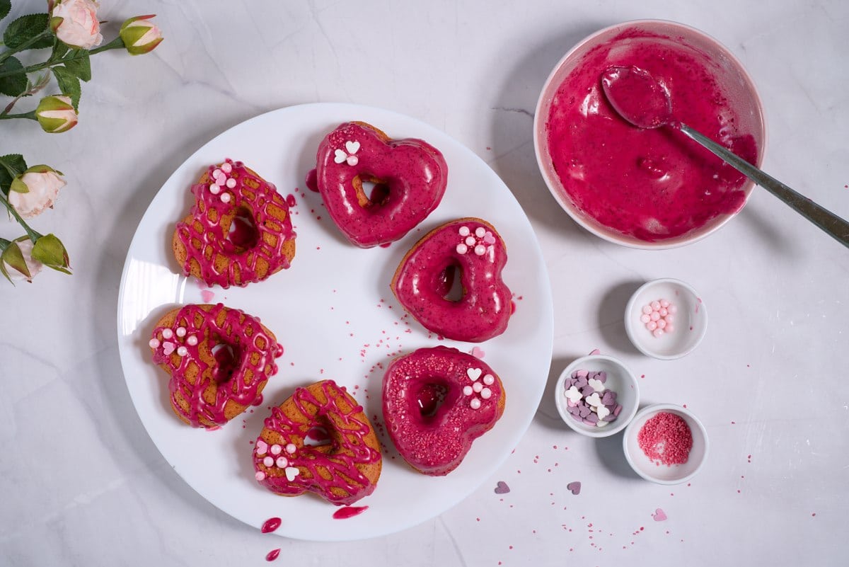 pinkillä tomusokerikuorrutteella ja syötävillä helmillä ja strösselillä koristellut donitsit.