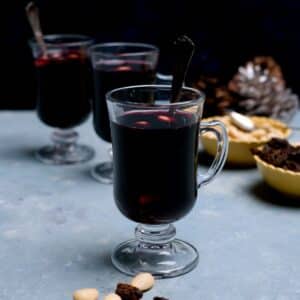 tumma viininpunainen juoma pienessä kahvallisessa lasissa ja edessä manteleista sekä rusinoita.