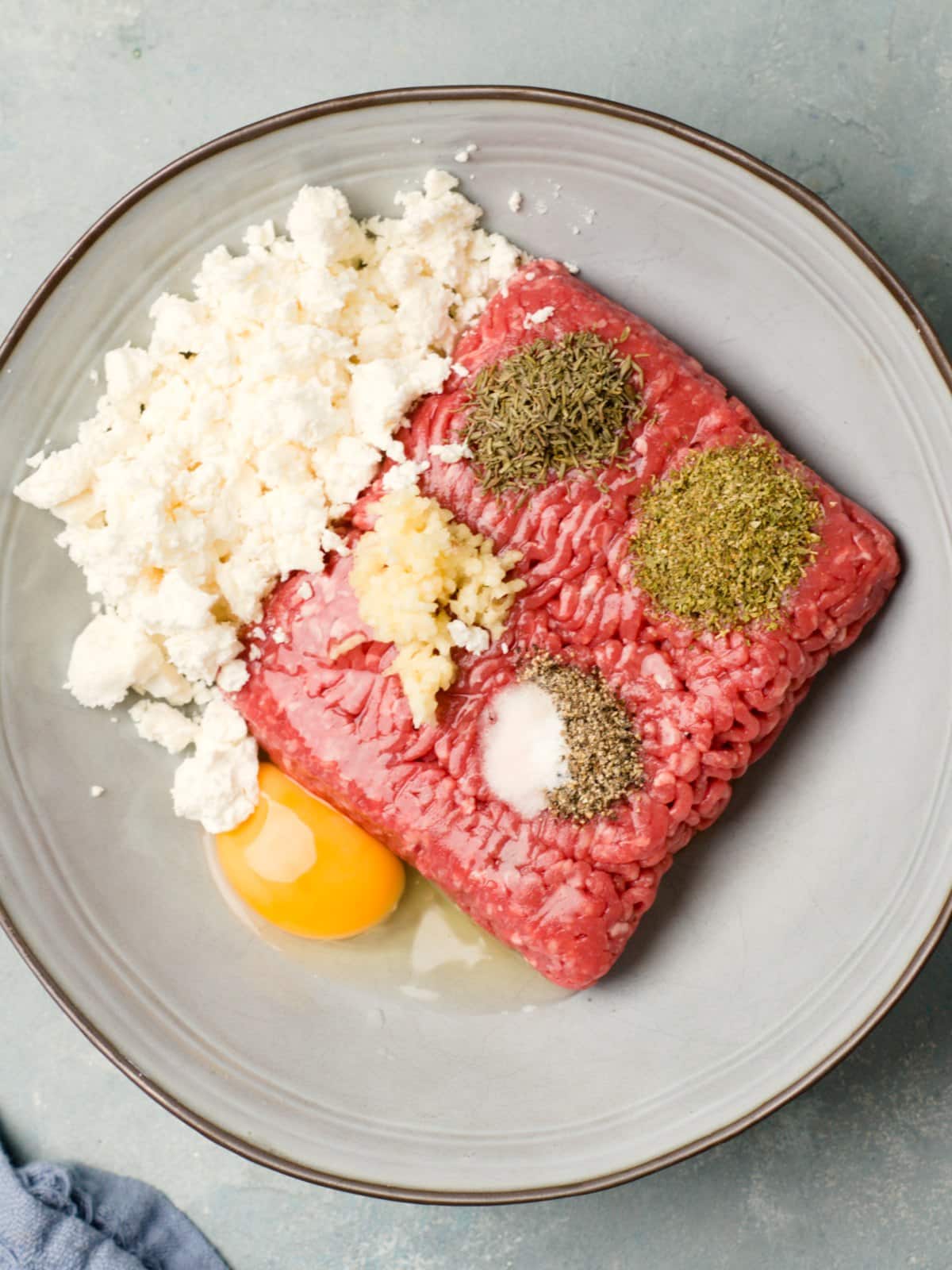 Lihapulla ainekset kulhossa, jauheliha, murusteltu feta, yrttejä, valkosipulia, kananmuna. 