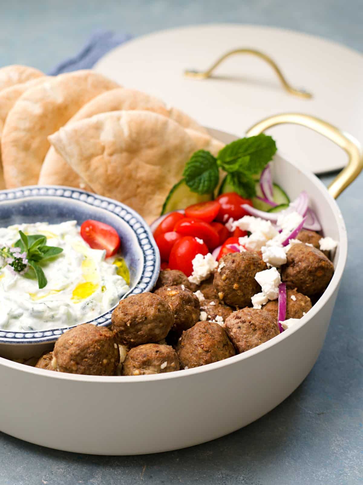 Lähikuva lihapullista joissa fetajuustoa valkoisessa kasarissa lisukkeiden kera. 